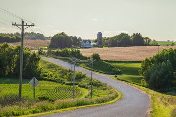 Northeast Iowa road and farm with power lines back lit at sunset on a spring day
