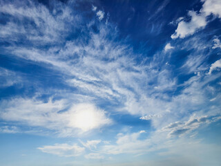 Ethereal Sky: Wispy Clouds and Sunlight. A breathtaking view of a vivid blue sky, adorned with delicate, wispy clouds diffusing the warm sunlight.