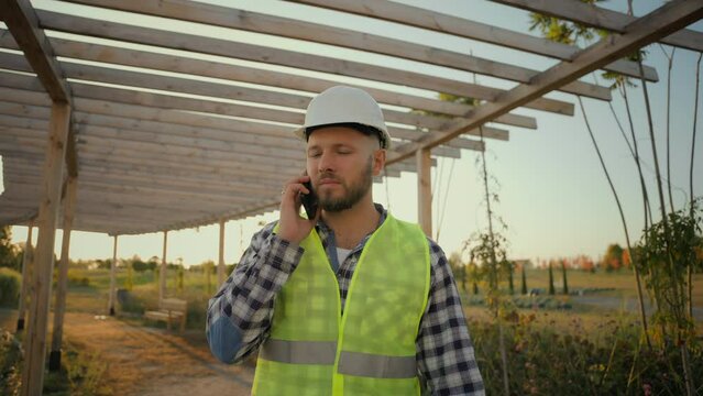 Experienced Caucasian man male guy uniform businessman specialist environmental engineer calling talking mobile phone smartphone call discuss business construction plan outside rural farmland village