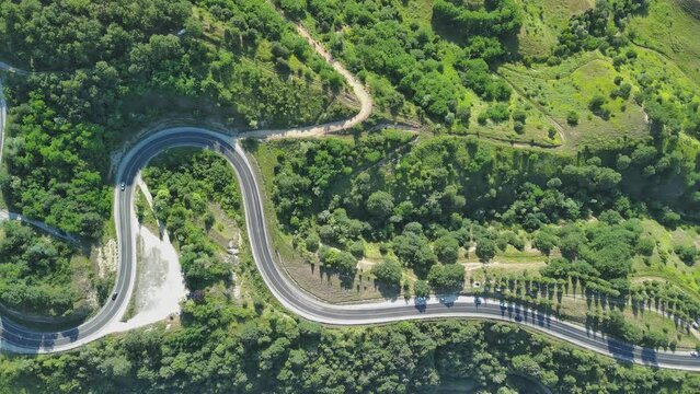 Aerial view of winding asphalt mountain road among green trees in summer.