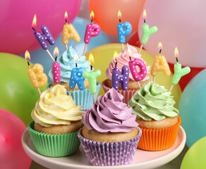 Birthday cupcakes with burning candles on stand near color balloons