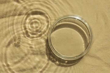 Stylish presentation for product. Glass podium in water on sand, top view. Space for text