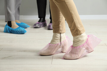Women wearing pink shoe covers onto different footwear indoors, selective focus