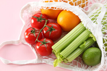String bag with different vegetables and fruits on pink background, closeup