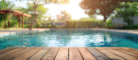 Wooden table is empty in foreground with a blurred swimming pool in the background