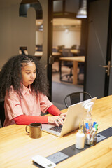 afro adult woman sitting and using laptop in coworking office interior