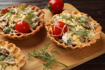 Tasty tartlets with cheese, tomatoes, mushrooms and dill on wooden table, closeup