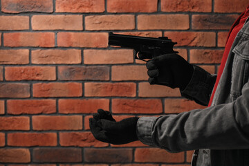 Armed robbery. Dangerous criminal with gun near brick wall, closeup. Space for text