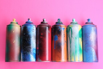 Many spray paint cans on pink background, flat lay