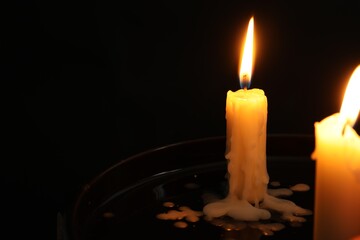 Two burning church candles on black background, space for text