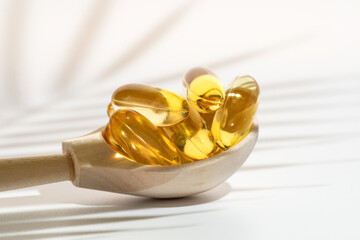 Golden omega 3 capsules in a wooden spoon on a striped surface