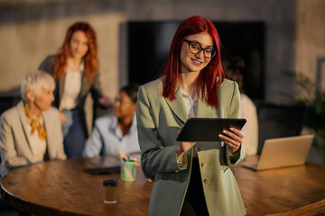 Female entrepreneur standing at office and smiling at the tablet.