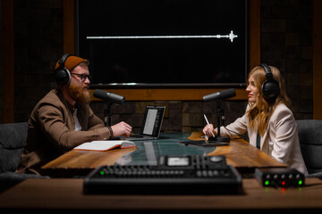 Two radio hosts talking and smiling while sitting near microphones in broadcasting studio