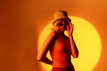 Stylish female model with light natural makeup wearing trendy sunglasses against orange background