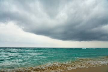 Waves and foam on a tropical sandy beach with clouds.