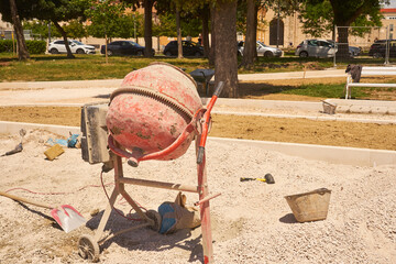 Concrete mixer in the sun with a park in the background.