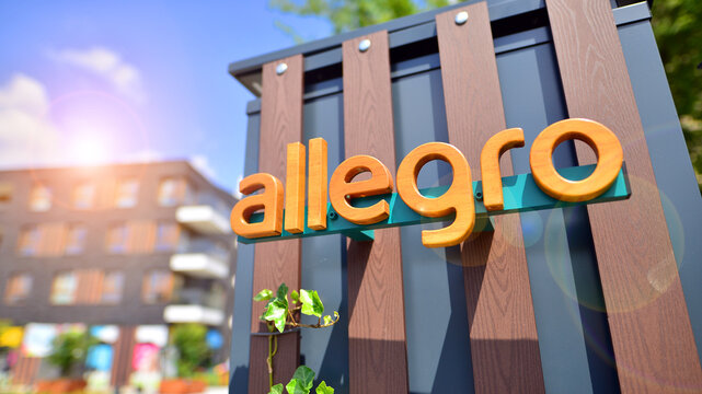 Warsaw, Poland. 8 June 2024. View of the Allegro Group logotype on the wooden wall with ivy. A modern residential building in the background.