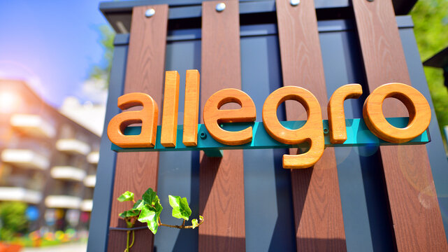 Warsaw, Poland. 8 June 2024. View of the Allegro Group logotype on the wooden wall with ivy. A modern residential building in the background.