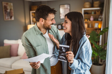 Happy pregnant woman with her husband watch ultrasound photo of baby