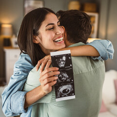Happy pregnant woman with her husband watch ultrasound photo of baby