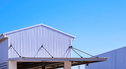 White aluminium corrugated steel workshop building with awning inside of factory area against blue sky background 