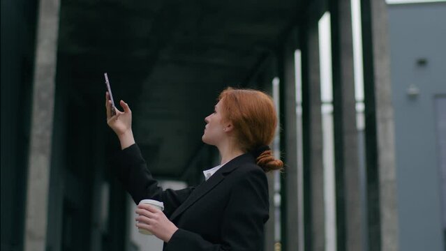 Worried young ginger Caucasian woman girl female student businesswoman suit rising hand mobile phone trying catch internet lost signal no wifi bad cellular connection trouble tech error outdoors city