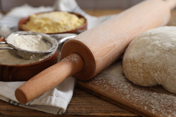 Rolling pin, flour and dough on wooden table, closeup