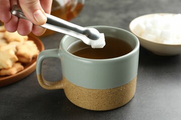 Woman adding sugar cube into aromatic tea at grey table, closeup