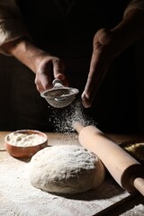 Man sprinkling flour over dough at wooden table, closeup