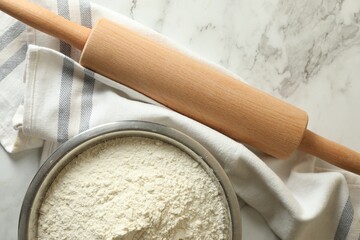 Flour in bowl, rolling pin and napkin on white marble table, top view