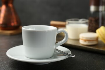 White espresso cup, spoon and saucer on dark textured table, closeup