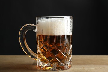 Mug with fresh beer on wooden table against black background, closeup