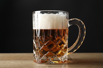 Mug with fresh beer on wooden table against black background, closeup