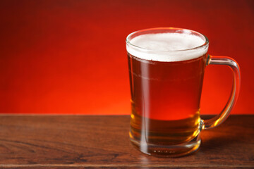 Mug with fresh beer on wooden table against red background. Space for text