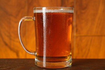 Mug with fresh beer on wooden table against color background, closeup