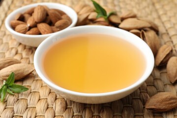 Almond oil in bowl, nuts and leaves on wicker table, closeup