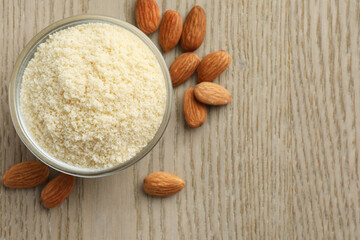 Fresh almond flour in bowl and nuts on wooden table, top view. Space for text