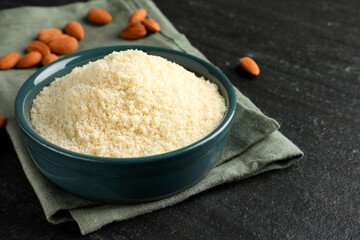 Fresh almond flour in bowl on dark textured table, closeup