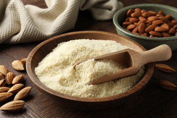 Fresh almond flour, scoop in bowl and nuts on wooden table, closeup