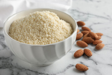 Fresh almond flour in bowl and nuts on white marble table, closeup