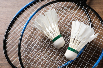 Feather badminton shuttlecocks and rackets on wooden table, above view