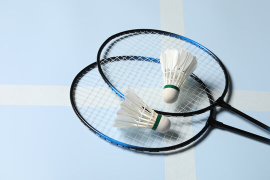 Feather badminton shuttlecocks and rackets on light blue background, closeup. Space for text
