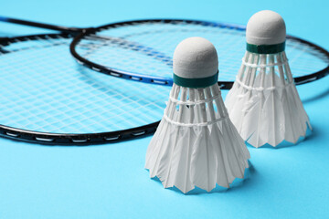 Feather badminton shuttlecocks and rackets on light blue background, closeup