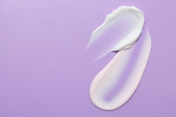 Samples of face cream on violet background, top view. Space for text