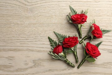 Many stylish red boutonnieres on light wooden table, flat lay. Space for text
