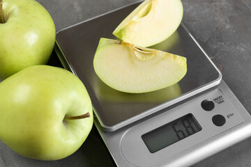 Kitchen scale with pieces of apple and fruits on grey textured table, closeup