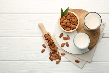 Glasses of almond milk and almonds on white wooden table, top view. Space for text