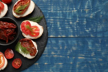 Delicious bruschettas with ricotta cheese, tomatoes, and dill on blue wooden table, top view. Space for text