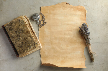 Sheet of old parchment paper, lavender flowers , vintage book and pocket chain clock on grey table,...
