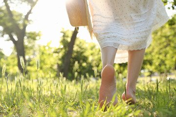 Woman with straw hat walking barefoot on green grass outdoors, closeup. Space for text